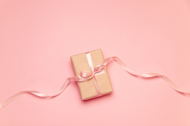 Craft present box with pink pastel bow ribbon on pink canvas background - 写真・画像