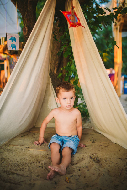 Téma nyári vakáció, kisfiú, kaukázusi gyermek játszik az erdős területen parkban a játszótéren a kertben. gyerek a Tipi Wigwam sátor nyáron. Fedezze fel és játsszon a természetben a nyári időfutam - Fotó, kép