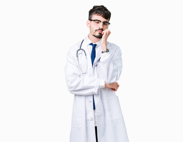 Νέος γιατρός άνδρας φοράει παλτό νοσοκομείο πάνω από απομονωμένες υπόβαθρο σκέψης ψάχνει κουρασμένη και τρυπημένο με προβλήματα κατάθλιψης με σταυρωμένα χέρια. - Φωτογραφία, εικόνα