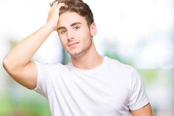Young handsome man wearing white t-shirt over isolated background Smiling confident touching hair with hand up gesture, posing attractive - Фото, зображення