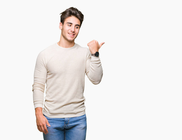 Young handsome man over isolated background smiling with happy face looking and pointing to the side with thumb up. - Photo, Image