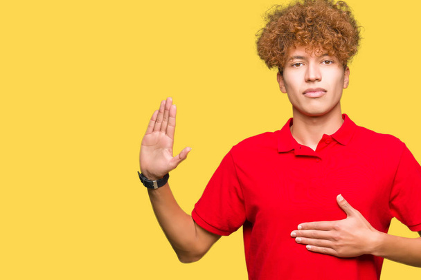 Joven hombre guapo con pelo afro vistiendo camiseta roja jurando con la mano en el pecho y la palma abierta, haciendo un juramento de lealtad promesa
 - Foto, imagen