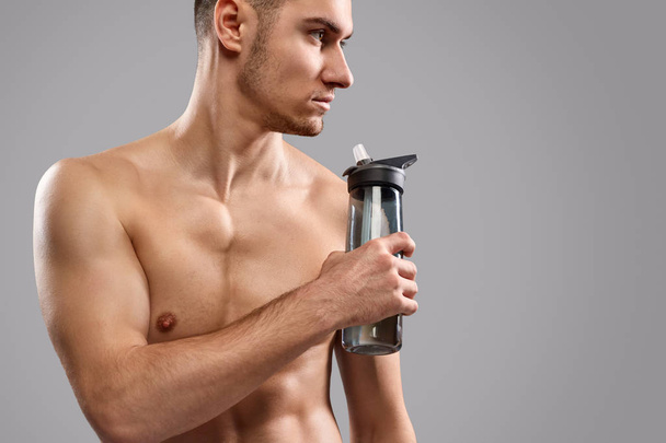 Shirtless sportsman drinking water and looking away - 写真・画像