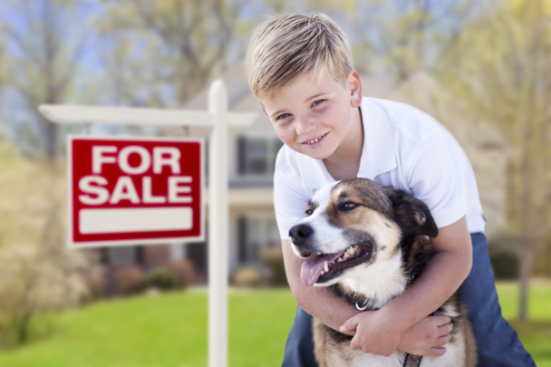 Joven niño y su perro en frente de en venta signo y casa
 - Foto, imagen