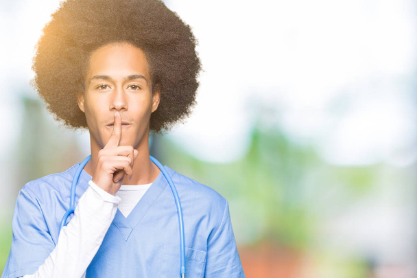 Молодий афроамериканець лікар людина з афро волосся просять бути спокійним з пальцем на губах. Тиша і таємне поняття. - Фото, зображення