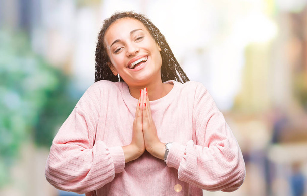 Jovem trançado cabelo afro-americano menina vestindo suéter sobre fundo isolado orando com as mãos juntas pedindo perdão sorrindo confiante
. - Foto, Imagem