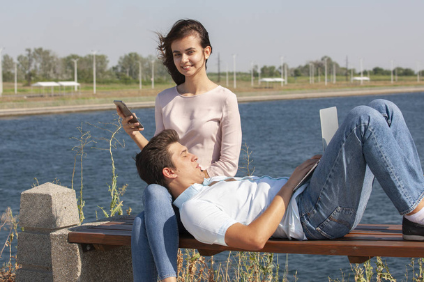 happy young couple using laptop while sitting together in park - Photo, image