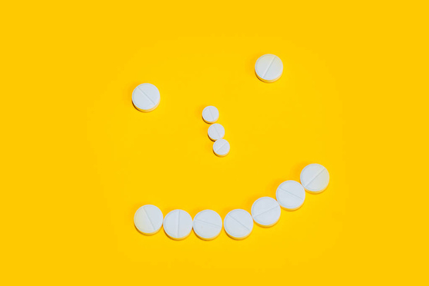 face with a smile laid out with pills and vitamins on a yellow background. view from above - Foto, immagini