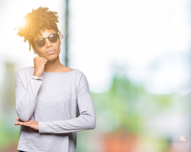 schöne junge afrikanisch-amerikanische Frau mit Sonnenbrille über isoliertem Hintergrund mit der Hand am Kinn, die über Fragen nachdenkt, nachdenklichen Ausdruck. Lächeln mit nachdenklichem Gesicht. Zweifelhaftes Konzept. - Foto, Bild