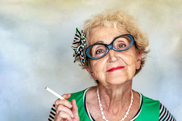 Old wrinkled fashionable woman in glasses with a cigarette in ha - Photo, Image