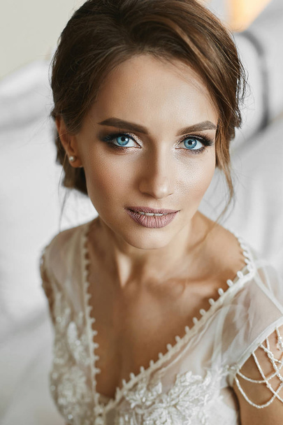 Beautiful brunette woman with wedding hairstyle, with bright makeup and with deep blue eyes. Portrait of the young beautiful bride in the morning - Valokuva, kuva