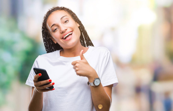 Young braided hair african american girl showing using smartphone over isolated background happy with big smile doing ok sign, thumb up with fingers, excellent sign - Φωτογραφία, εικόνα