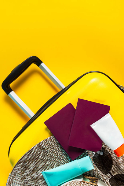 Яскрава та стильна валіза розміру кабіни з солом'яним капелюхом, сонцезахисним кремом та паспортами
 - Фото, зображення
