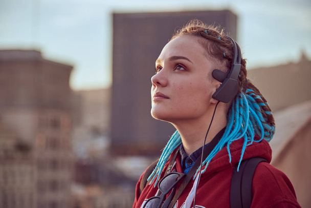 A young girl with blue dreadlocks listening to music in the city. - Foto, imagen