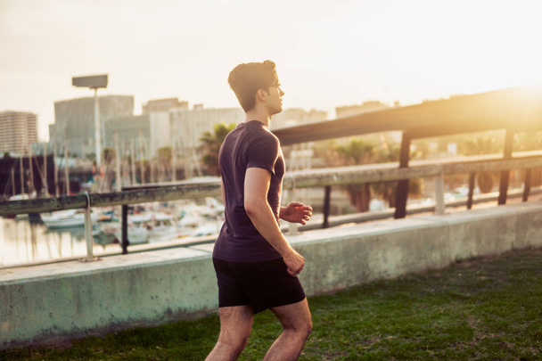 Young athletic man running at park with skyscrapers background - Fotoğraf, Görsel