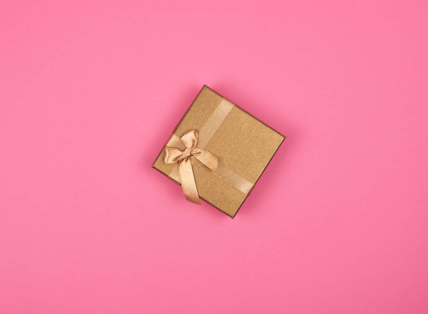 gesloten gouden geschenk doos met een strik op een roze achtergrond - Foto, afbeelding