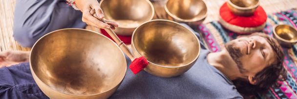 BANNER, LONG FORMAT Nepal Buddha copper singing bowl at spa salon. Young beautiful man doing massage therapy singing bowls in the Spa against a waterfall. Sound therapy, recreation, meditation - Φωτογραφία, εικόνα