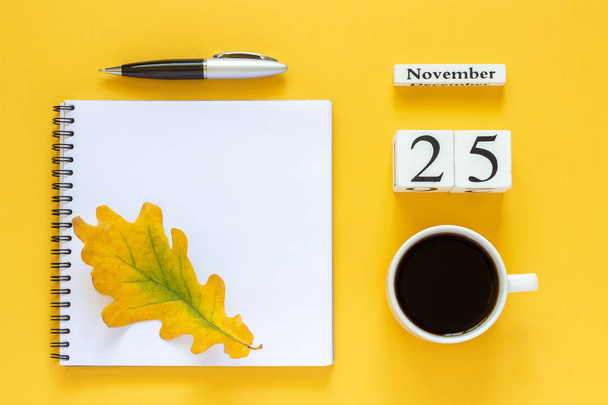 calendar November 25 cup of coffee, notepad with pen and yellow leaf on yellow background - Fotografie, Obrázek