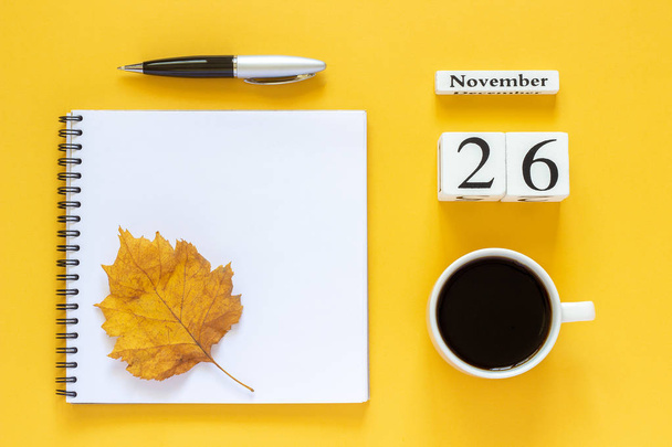 calendar November 26 cup of coffee, notepad with pen and yellow leaf on yellow background - Valokuva, kuva