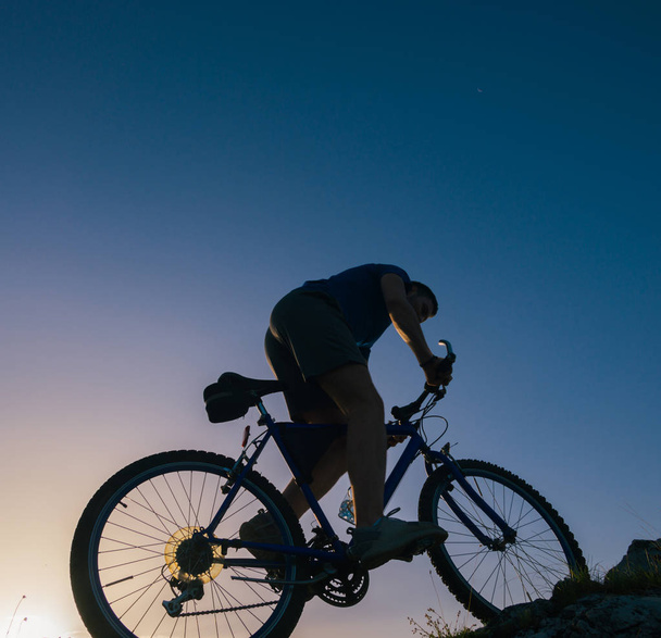 Silueta de un ciclista de montaña macho en forma montando su bicicleta cuesta arriba o
 - Foto, imagen
