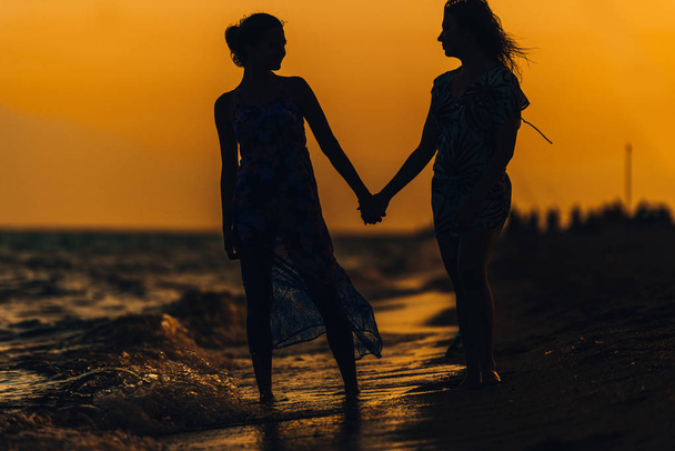 Retrato de mujeres jóvenes como silueta mientras sostienen junto al mar
 - Foto, Imagen