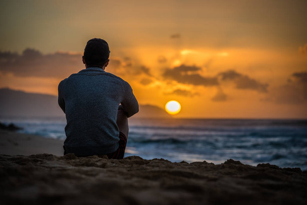 Silhouette de jeune homme caucasien assis sur Sunset Beach à Hawaï regardant le coucher du soleil sur l'océan
 - Photo, image