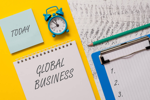 Conceptual hand writing showing Global Business. Business photo showcasing Trade and business system a company doing across the world Spiral notepad sheet marker alarm clock wooden background. - Photo, Image