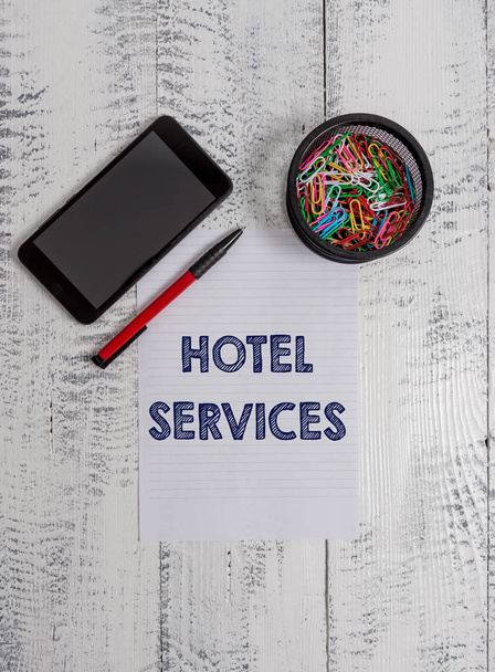 Conceptual hand writing showing Hotel Services. Business photo text Facilities Amenities of an accommodation and lodging house Smartphone paper sheet clips ballpoint wooden vintage background. - Photo, Image