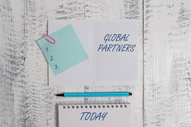 Word writing text Global Partners. Business concept for Two or more firms from different countries work as a team Open squared spiral notepad clip note highlighter lying old wooden background. - Photo, Image