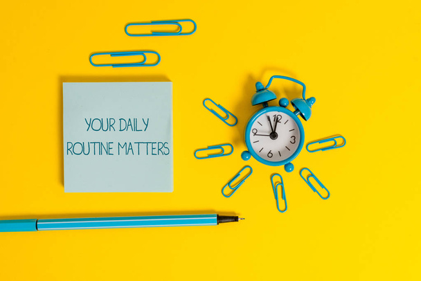 Word writing text Your Daily Routine Matters. Business concept for practice of regularly doing things in fixed order Metal alarm clock wakeup clips ballpoint notepad colored background. - Photo, Image