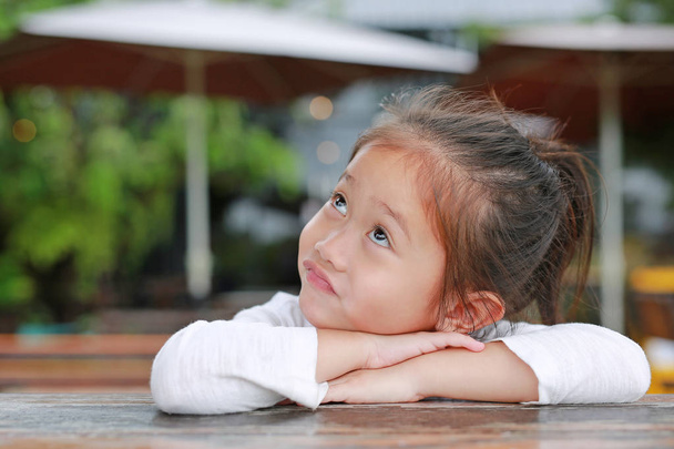 Komik surat ahşap masanın üzerinde yatan şımarık küçük Asyalı çocuk kızla. - Fotoğraf, Görsel