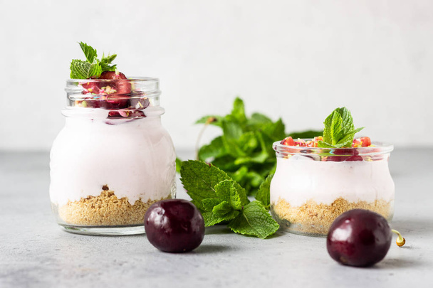 No baked cheesecake with cherry in glass jars, fresh cherries and mint on a grey stone background. Healthy dessert. Copy space. - Φωτογραφία, εικόνα