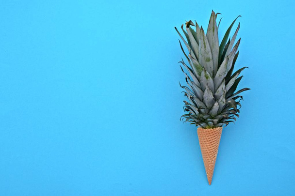 De stengel van een ananas in een ijsje tegen een monochrome achtergrond als een symbool van ananas-ijs als een fruitige verfrissing in de zomer - Foto, afbeelding