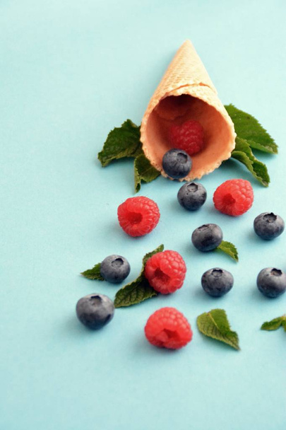 An ice cream cone with blueberries, raspberries and mint on a colorful background as a symbol of a refreshing summer fruity ice cream - Foto, Imagem