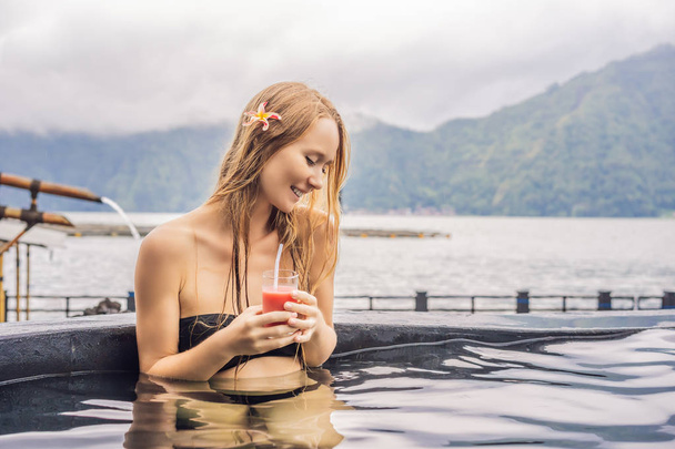 Geothermal spa. Woman relaxing in hot spring pool against the lake. hot springs concept. Drinking guava juice - 写真・画像