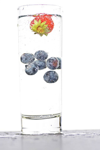 капли черники и клубники в стакан, полный газированной воды - закрыть на изолированном стекле
 - Фото, изображение