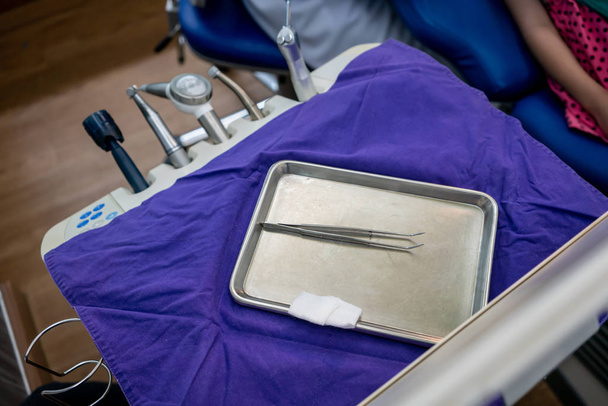 Ιατρικό τσιμπιδάκι από ανοξείδωτο χάλυβα στο τραπέζι της πολυθρόνας. - Φωτογραφία, εικόνα