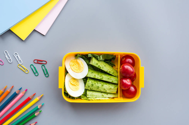 School supplies and lunch box with sandwich and vegetables. Back to school. Healthy eating habits concept - background layout with free text space. Flat lay composition, mockup, top view - Foto, afbeelding