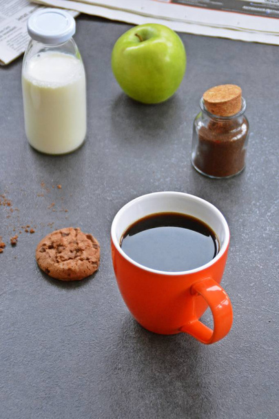 Café en una taza de naranja sobre una mesa con manzanas, leche, azúcar y una galleta
  - Foto, Imagen