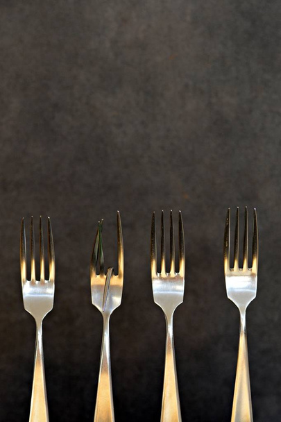 Drie normale en een gebogen vork in een rij als symbool dat uitzonderlijk is, is niet gelijk aan nuttig en zinvol-concept met vorken-één is anders dan alle andere  - Foto, afbeelding