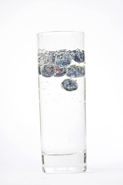 Ρίξτε βατόμουρα σε ένα ποτήρι γεμάτο ανθρακούχο νερό-κοντά σε ένα απομονωμένο γυαλί  - Φωτογραφία, εικόνα