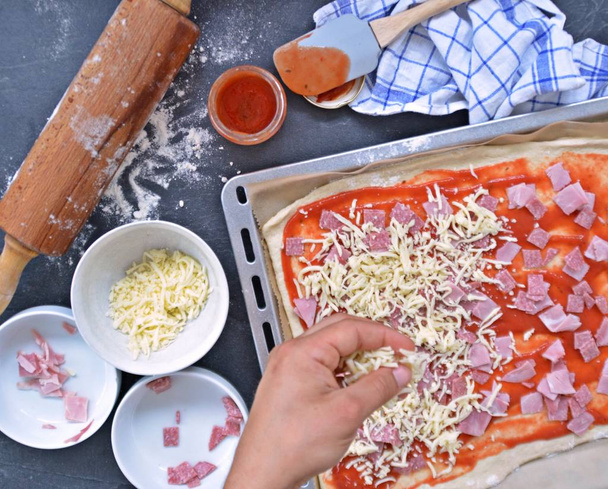 Yakın çekim-Man, jambon, salam ve peynir pişirme levha yanında malzemeler ile pizza hamur dolu bir pizza dolduruyor  - Fotoğraf, Görsel