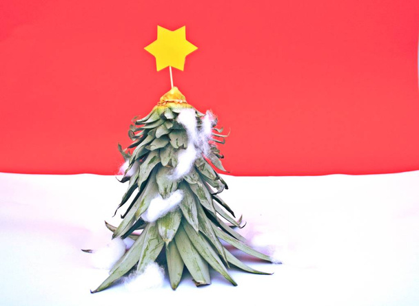 Ein Ananasstiel wird zum Weihnachtsbaum mit gelbem Stern darauf - Konzept für Weihnachten mit Platz für Text oder Elemente vor monochromem Hintergrund  - Foto, Bild