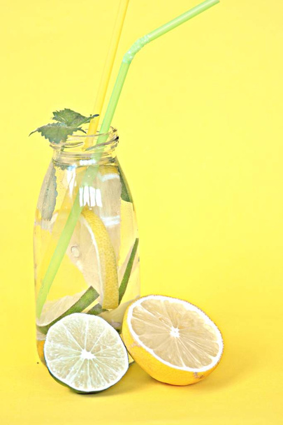 Zitronen-, Minz- und Limettenstücke in einer Flasche voll Wasser als fruchtige Erfrischung im Sommer vor schlichtem Hintergrund - Foto, Bild