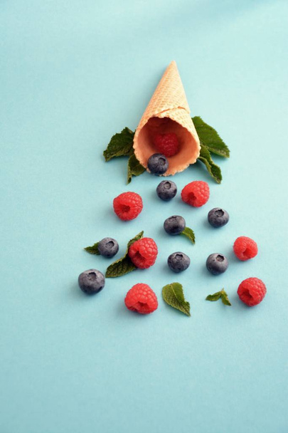 An ice cream cone with blueberries, raspberries and mint on a colorful background as a symbol of a refreshing summer fruity ice cream - Fotoğraf, Görsel