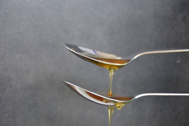 Miel fluye sobre cuchara sobre fondo negro - Foto, Imagen