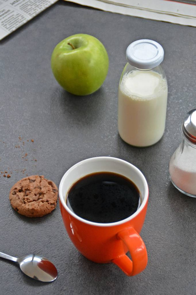 Café en una taza de naranja sobre una mesa con manzanas, leche, azúcar y una galleta
  - Foto, Imagen