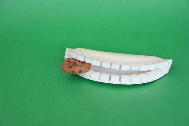 Zähne aus Zuckerwürfeln, die vor buntem Hintergrund in einen Keks beißen  - Foto, Bild