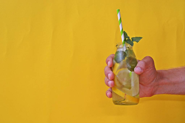 Holding a glass full of ice, limes, lemons and mint in your hand - a perfect match for the soul on a colorful background with space for text or other elements  - Photo, Image