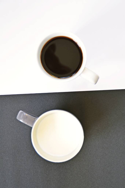 Dos tazas delante de un fondo medio negro y medio blanco, una taza contiene café, la otra leche y ambos crean un contraste, concepto para yin y yang con tazas de café
 - Foto, imagen